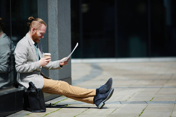 Positiivinen menestyvä hipsteri nuori lakimies, jolla on parta ulkona istumassa ja lukemassa papereita valmistellessaan oikeudenkäyntiä
 - Valokuva, kuva