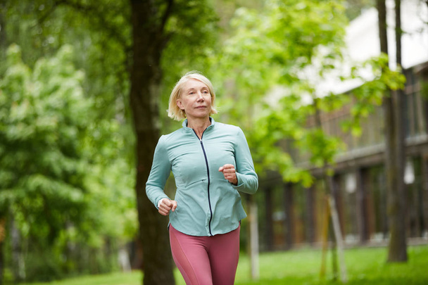 Desportista ativo loira saudável desfrutando correr de manhã em ambiente natural entre árvores verdes
 - Foto, Imagem
