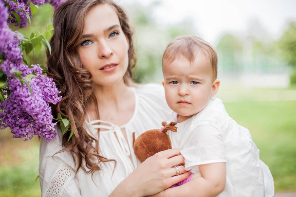 Bela jovem mãe e filha perto do lilás florescente. Primavera
. - Foto, Imagem