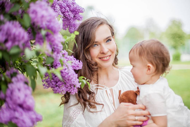 Hermosa joven madre e hija cerca de la floreciente lila. Primavera
. - Foto, Imagen