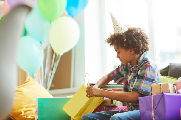 Ritratto vista laterale di felice afro-americano ragazzo apertura regali alla festa di compleanno, spazio copia
 - Foto, immagini