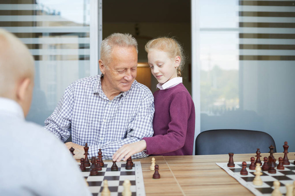 Petite fille aux cheveux roux tressés aidant son grand-père à gagner le jeu d'échecs contre son frère
 - Photo, image
