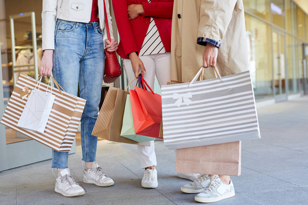 Close-up of unrecognizable stylish girls standing on street and holding paper bags with many purchases after shopping - Photo, Image