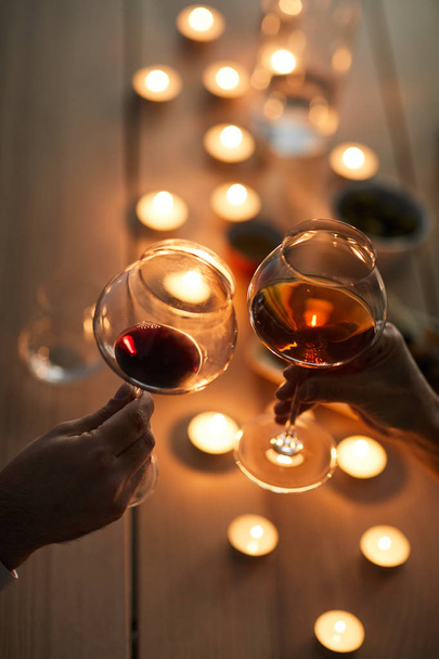 Primer plano de pareja irreconocible disfrutando de una cena romántica tintineando copas de vino y por mesa de madera iluminada por la luz de las velas, espacio para copiar
 - Foto, imagen