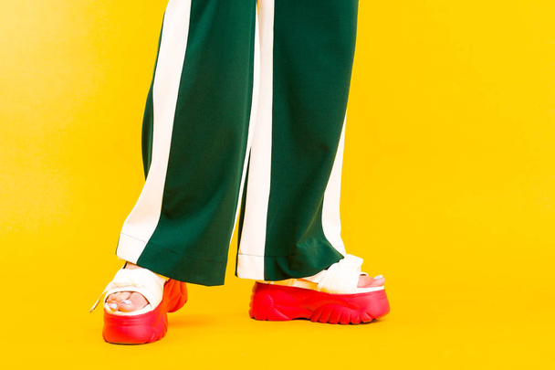 Ženský nohy ve sportovních sandálech s červenými podrážkami a zelenými kalhotami - Fotografie, Obrázek