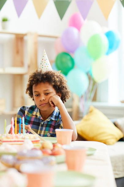 Portrait of sad African-American boy sitting at table alone during Birthday party, copy space - Photo, image