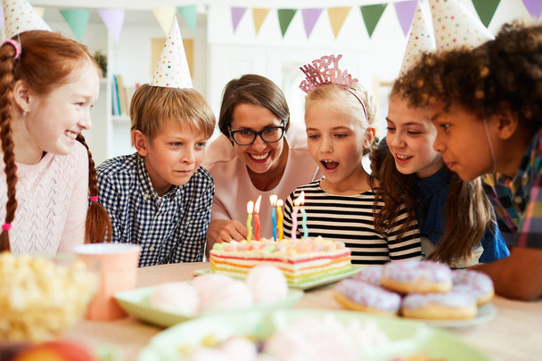 Portret van Happy Little Girl waait kaarsen op verjaardagstaart tijdens het feest met vrienden, kopieer ruimte - Foto, afbeelding