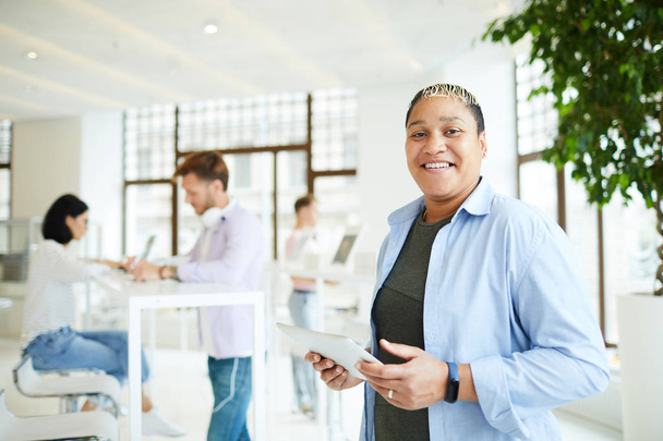Ritratto di giovane donna afro-americana felice eccitata in abbigliamento maschile in piedi allo spazio di coworking e utilizzando l'app mobile su tablet
 - Foto, immagini