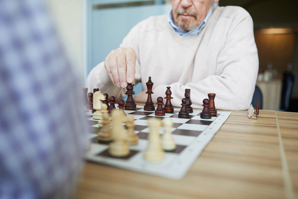 Ikääntynyt kokenut ammattilaissuurmestari, jolla on harmaa parta pelaamassa shakkia vastustajan kanssa tarkastetussa paidassa
 - Valokuva, kuva