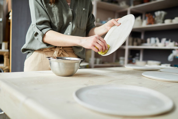 Портрет незамеченной молодой женщины, готовящей керамическую тарелку ручной работы в мастерской, копировальное пространство
 - Фото, изображение