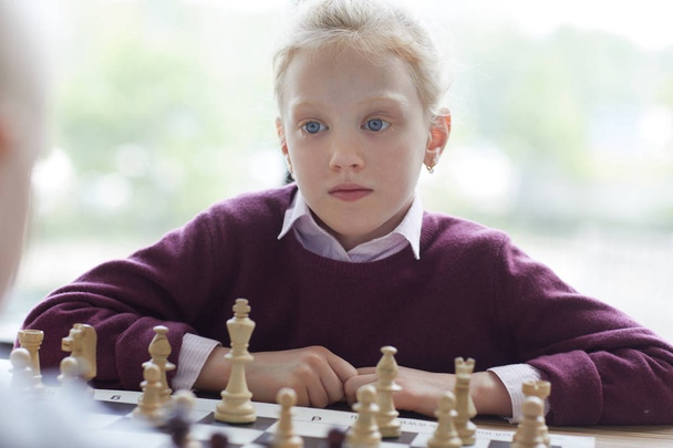 Ragazza dagli occhi blu con i capelli rossi in maglione viola giocare a scacchi e guardando attentamente la sua mossa avversario
 - Foto, immagini