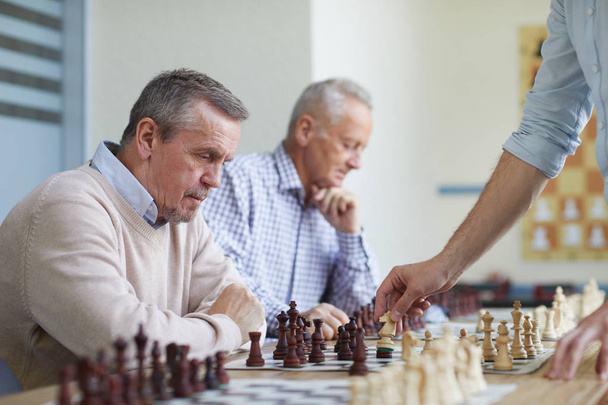 zwei ältere Männer mit silbernen Haaren verbringen ihre Freizeit im Schachclub, indem sie mit dem örtlichen Großmeister Schach spielen - Foto, Bild