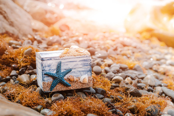 Pecho decorativo de madera con conchas marinas y estrella azul en la costa del mar
. - Foto, imagen