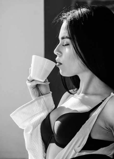 Sip of creamy cappuccino. Morning ritual. Girl sexy breasts drinking coffee near windowsill. Attractive female lingerie relaxing at home. Perfect coffee time. But first coffee. Tranquility and peace - Photo, Image