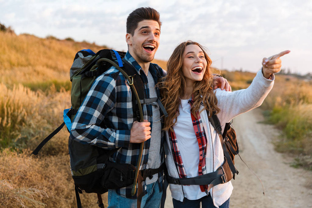 Cheerful young couple carrying backpacks hiking together - Фото, изображение