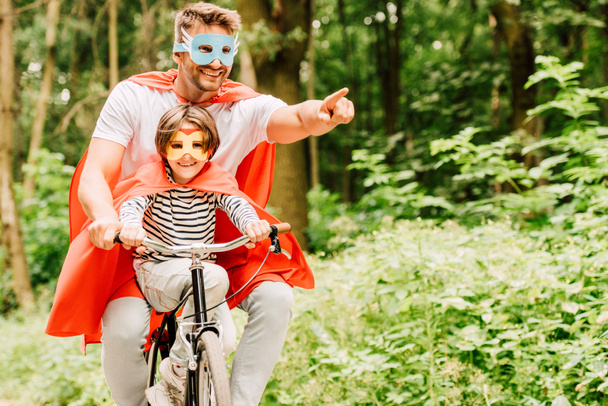 padre y niño montar en bicicleta alrededor del bosque en trajes de superhéroe
  - Foto, Imagen