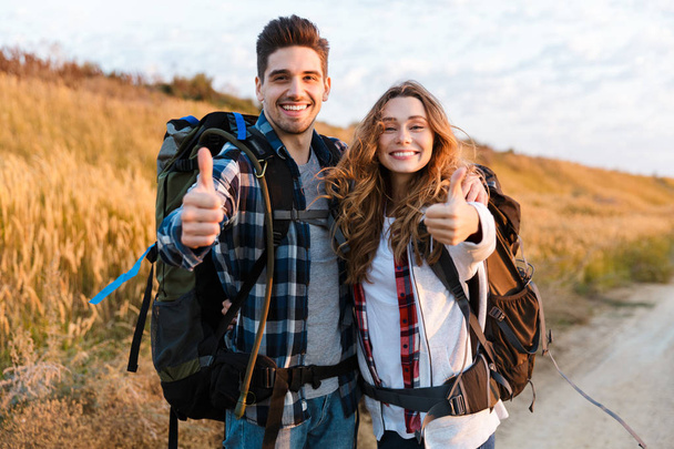 Cheerful young couple carrying backpacks hiking together - Фото, зображення