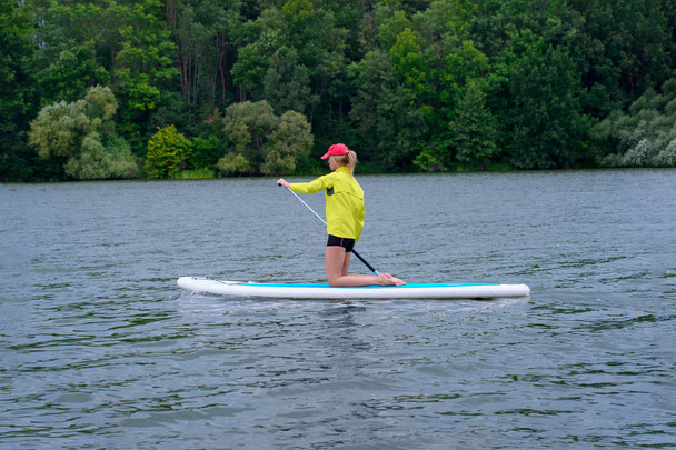 Young girl paddling on SUP board on a calm lake at city. Sup sur - Photo, Image