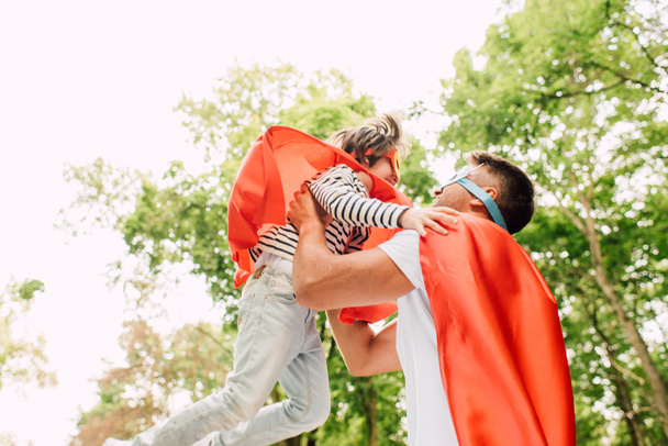 pai no traje de super-herói pegando filho com as mãos
 - Foto, Imagem