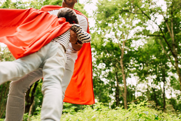 low angle view of father spinning little boy in red superhero cloak - Foto, Bild