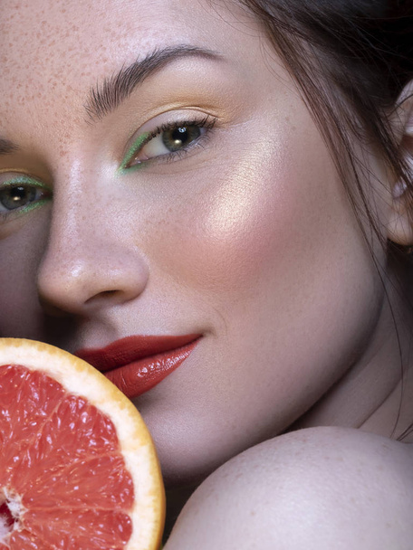 Pretty brunette woman with green creative make up and grapefruit - Zdjęcie, obraz