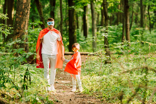 pełny widok długości ojca i syna stojącego w kostiumach superbohaterów w lesie - Zdjęcie, obraz