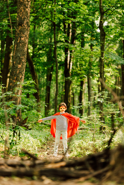 selective focus of small boy in superhero costume and mask standing in forest  - Fotó, kép