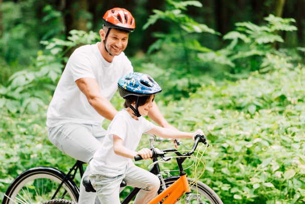 padre e hijo montando bicicletas mientras papá mira al niño
 - Foto, Imagen