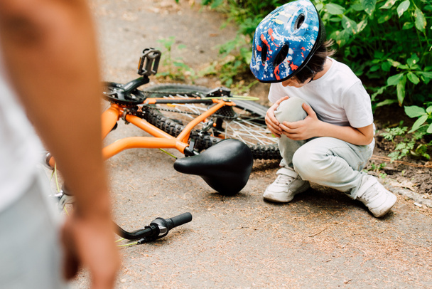 enfoque selectivo del niño cayó de la bicicleta y mirando a la rodilla mientras el padre de pie cerca de su hijo
 - Foto, Imagen