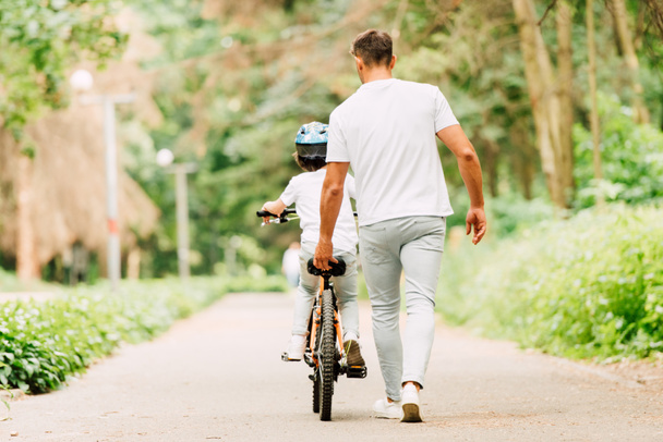 vista trasera del padre ayudando a su hijo a montar sosteniendo sentarse de bicicleta
 - Foto, Imagen