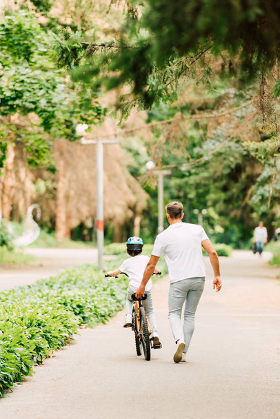 vista completa del padre ayudando a su hijo a montar con la celebración de sentarse de bicicleta
 - Foto, imagen