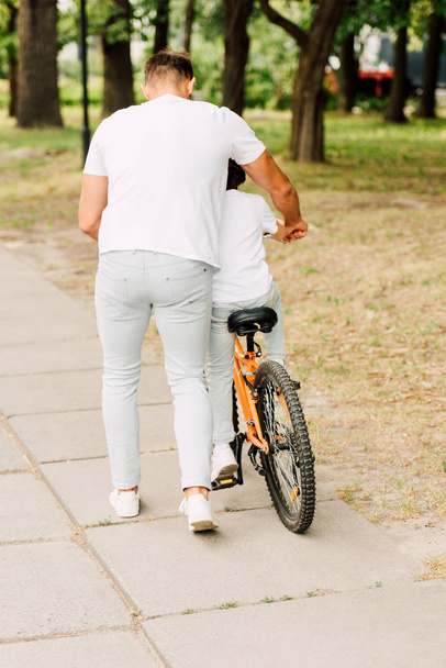 full length view of son riding bicycle while father helping boy - Fotoğraf, Görsel