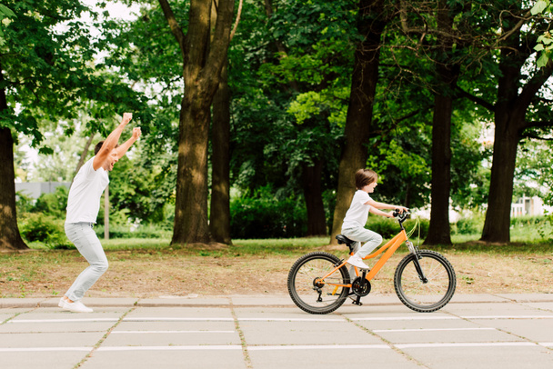 side view of happy father cheering son while kid riding bicycle - Photo, Image