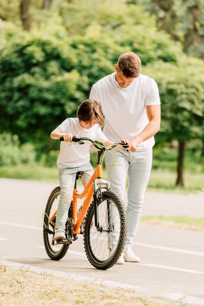 повна довжина зору батька дивлячись на сина в той час як дитина їзда на велосипеді - Фото, зображення