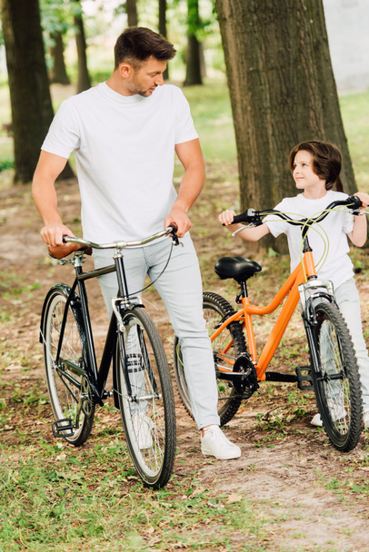 pełny widok długości ojca i syna chodzenie w parku z rowerami i patrząc na siebie - Zdjęcie, obraz