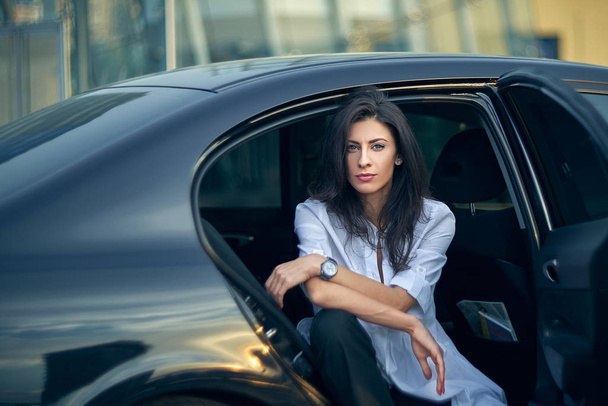 Serious woman sitting in the car over modern office facade - 写真・画像
