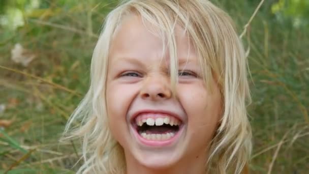 Portré egy aranyos mosolygott, és nevetni kékszemű szőke hét éves lány egy piszkos arc gyermek az utcán a városon kívül egy nyári napon - Felvétel, videó