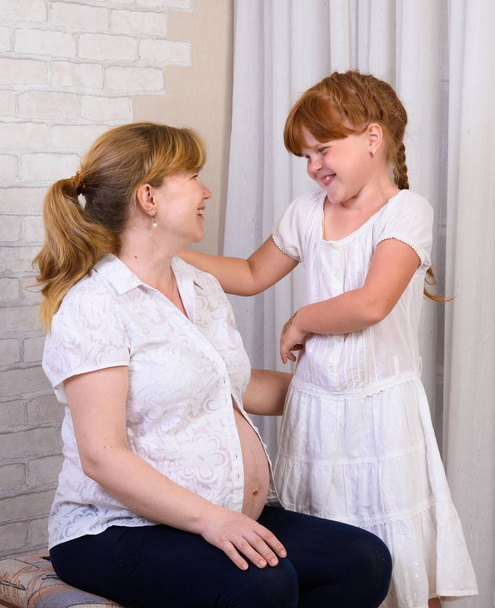 Little red-haired girl lifts pregnant mom - Photo, Image