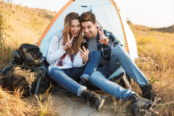 Cheerful young couple camping, sitting - Φωτογραφία, εικόνα