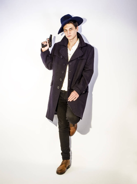 A shot of a young man in a coat with a gun on a light background - Foto, Imagen