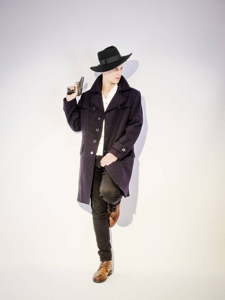 A shot of a young man in a coat with a gun on a light background - 写真・画像