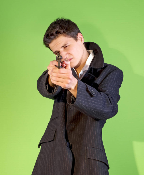 Handsome young man aiming a gun at the camera. - Foto, afbeelding