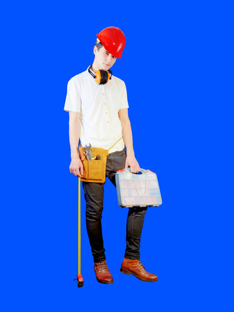 Young man in working clothing and protective helmet with equipment for repair and construction. Carpenter industry. Blue background - Φωτογραφία, εικόνα