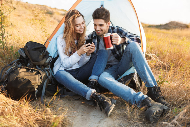 Cheerful young couple camping, sitting - Фото, изображение