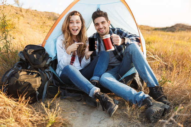 Happy young loving couple outside in free alternative vacation camping drinking hot tea. - Фото, изображение