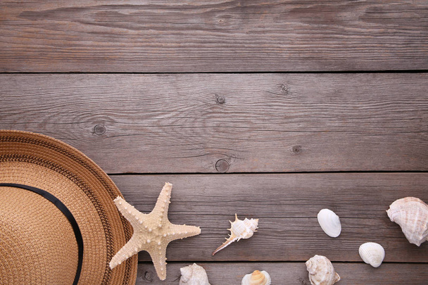 Beach hat with seashells on grey wooden table - Фото, изображение