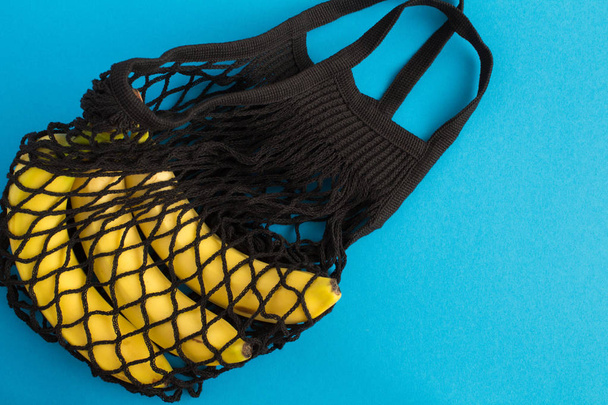 No plastic bag concept. Mesh shopping bag with  bananas on the blue background. Top view. Copy space. - Fotografie, Obrázek
