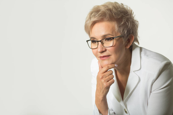 retrato de uma mulher adulta com um corte de cabelo curto usando óculos em uma jaqueta branca em um fundo branco
 - Foto, Imagem