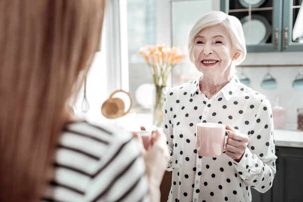 Cheerful senior woman smiling while standing with tea and talking - 写真・画像