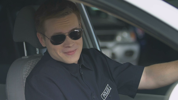 verantwortlicher Polizist mit Sonnenbrille sitzt im Streifenwagen und lächelt in die Kamera - Filmmaterial, Video